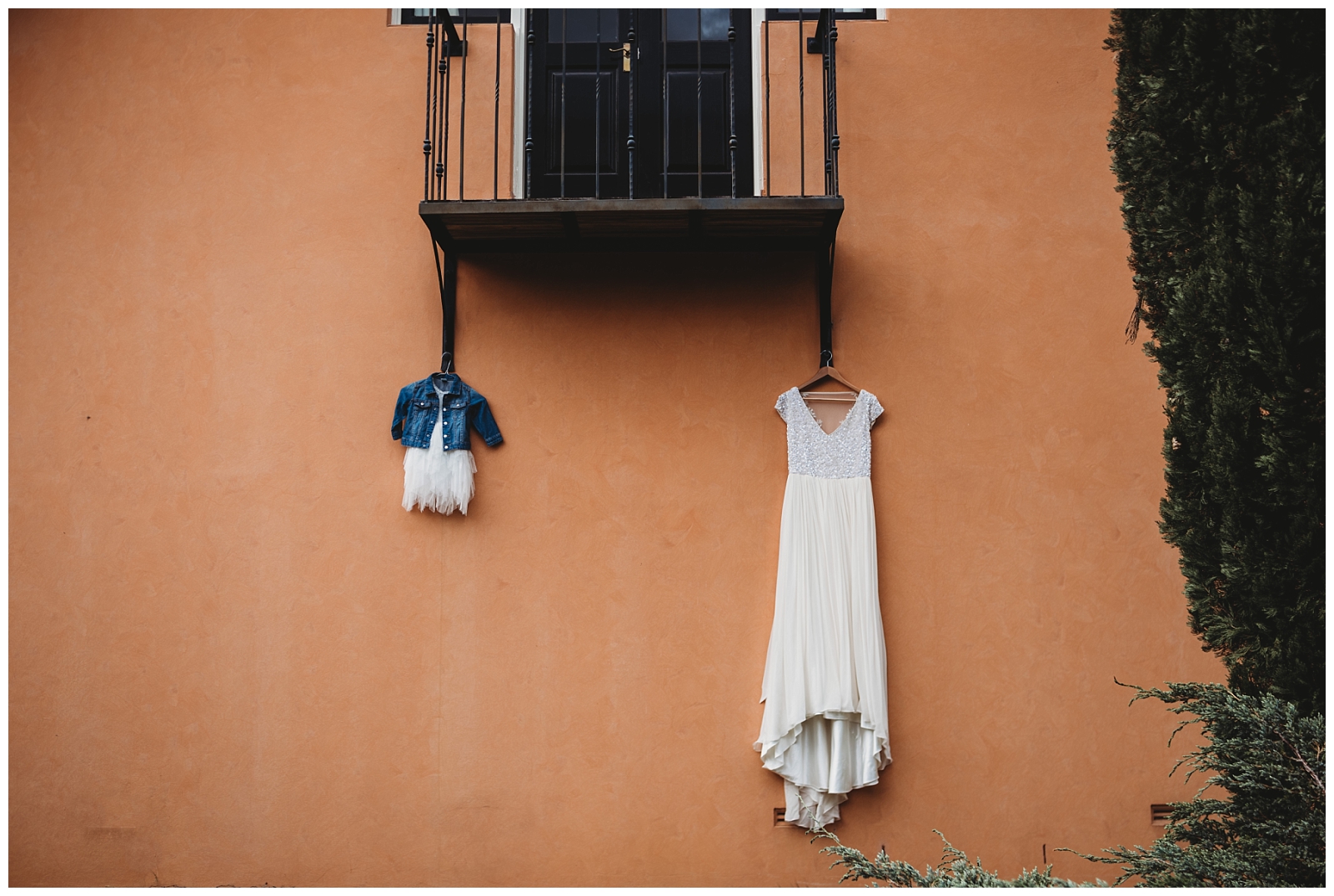 Bride and flower girls dress hanging off balcony in front of an orange wall.