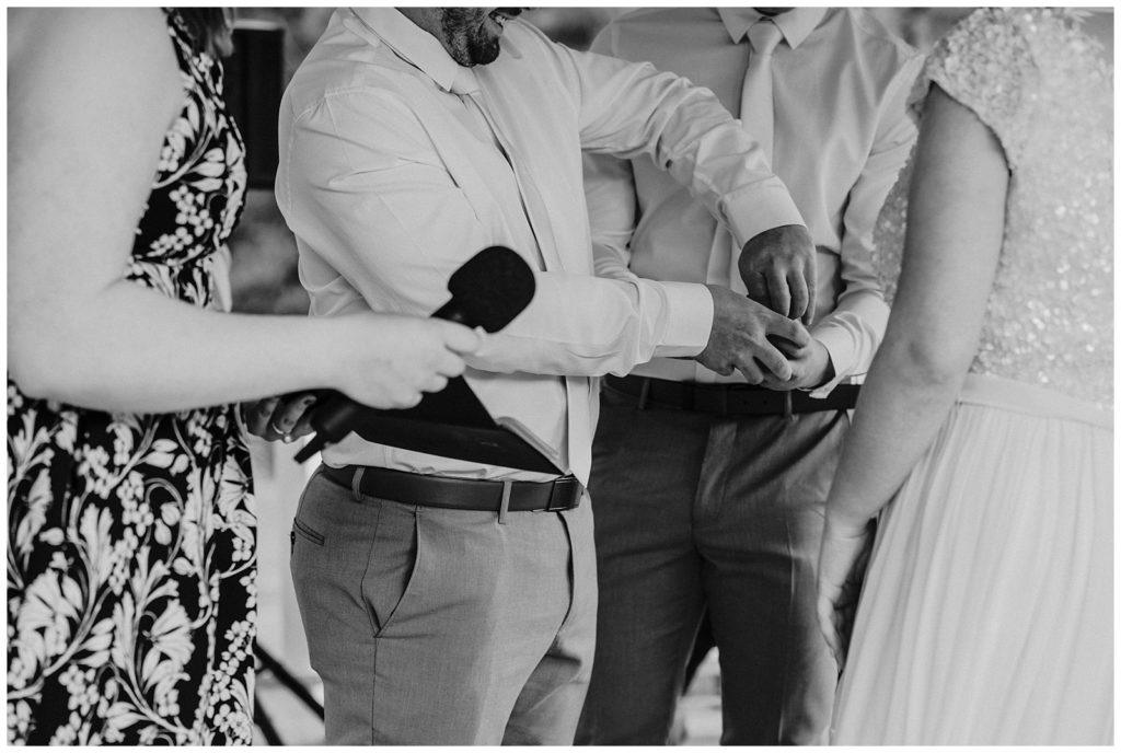 Black and white image groom taking rings  from ring box held by bestman.