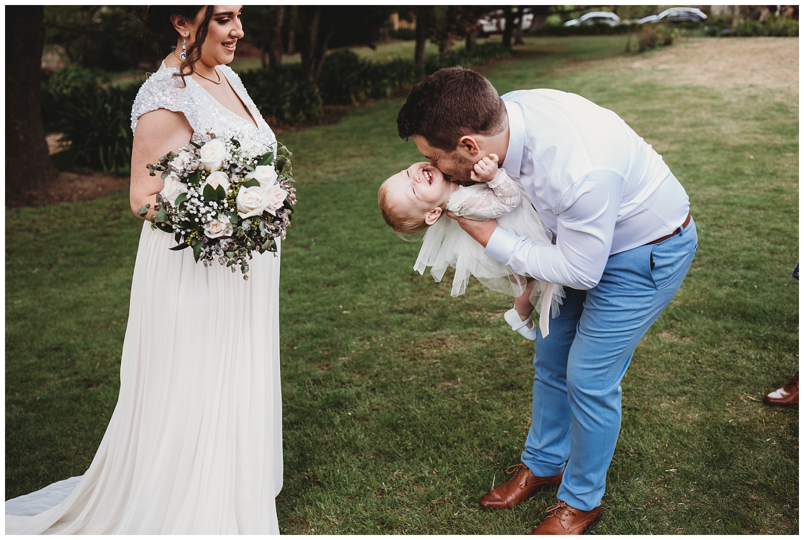 Bride watched as Groom tips their daughter upside down to make her giggle.