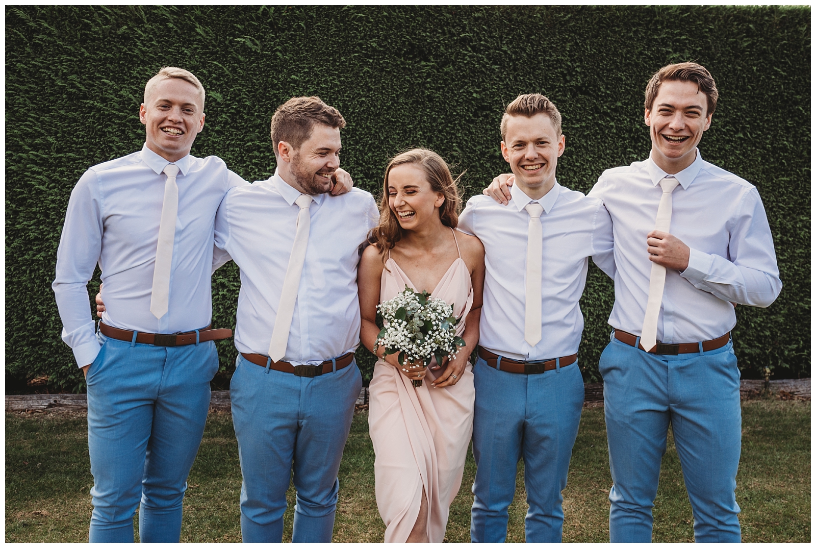 Groom stands with brothers and sister laughing.