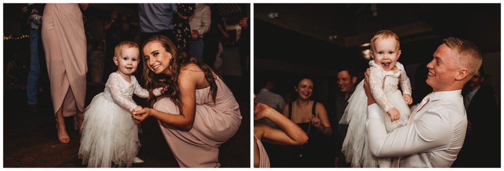 Flower girl poses for photo on dance floor with bridesmaid. Groomsman picks up flower girl and raises her above his head. 